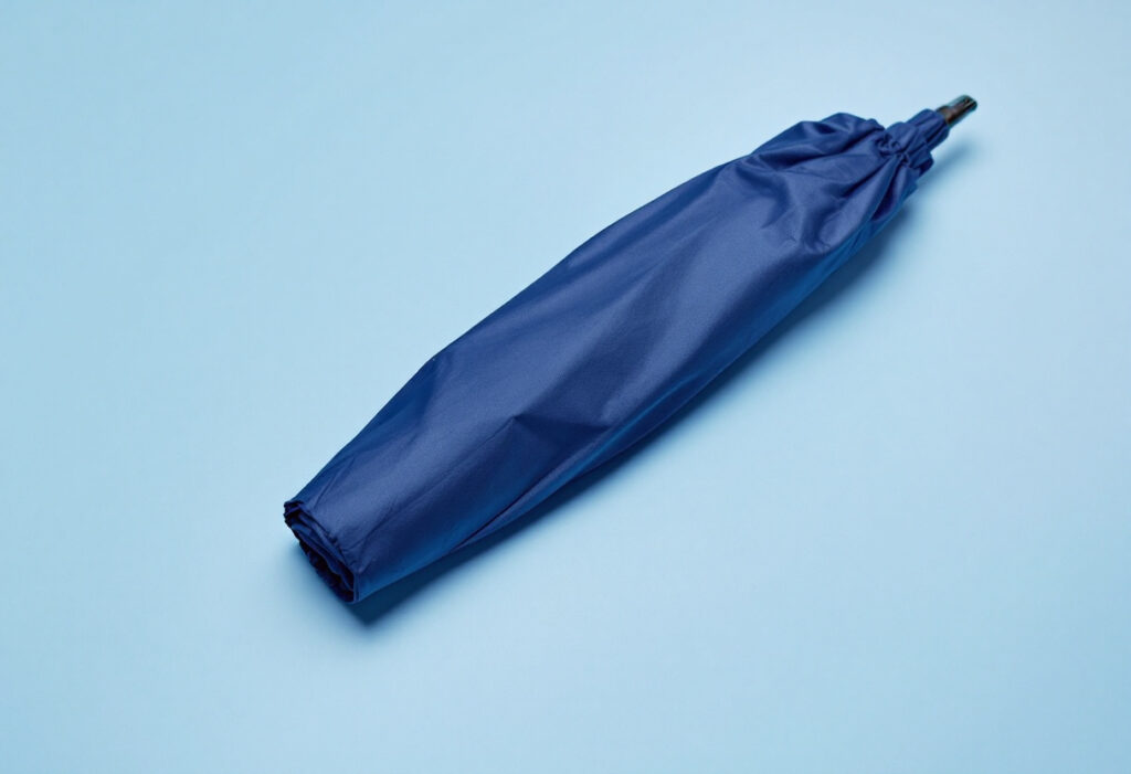 Parapluie bleu marine fermé posé à plat sur un fond bleu clair
