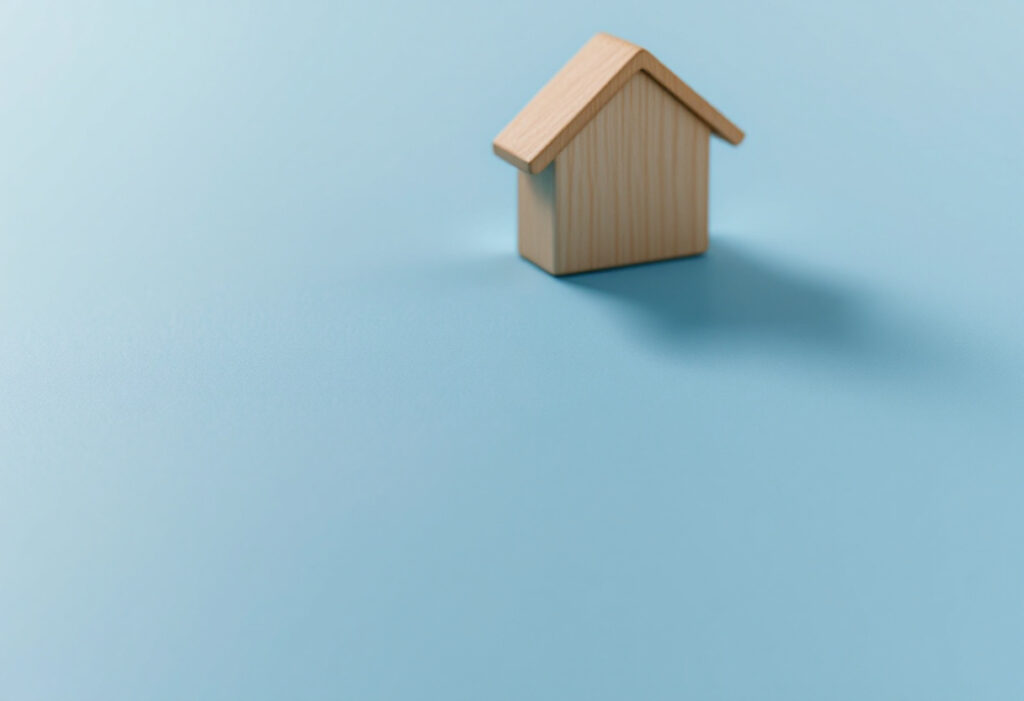 Clé en laiton posée à côté d'un petit bloc de bois clair en forme de maison, sur fond bleu clair